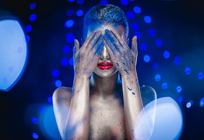 Naked woman with glitter covering her eyes against blue background