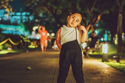 Cute girl standing on illuminated footpath at night