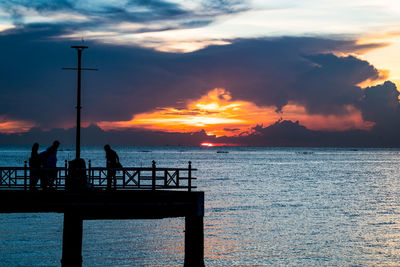 Silhouette people on pier by sea against sky during sunset