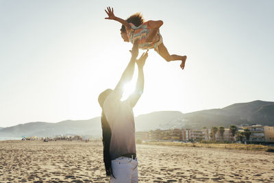 Playful father throwing daughter in air at beach