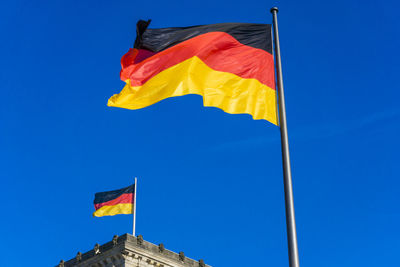 Low angle view of german flag on reichstag building against clear blue sky during sunny day