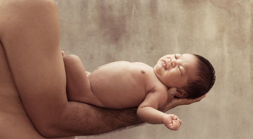 Midsection of shirtless father holding newborn son against wall