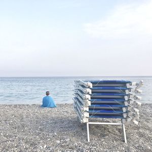 Rear view of man sitting on beach against sky