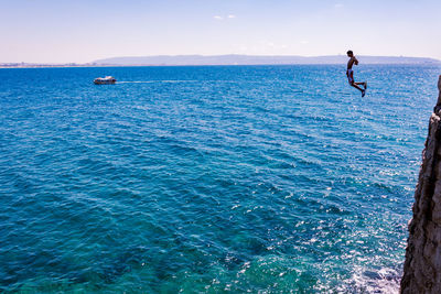 Man jumping off cliff into sea