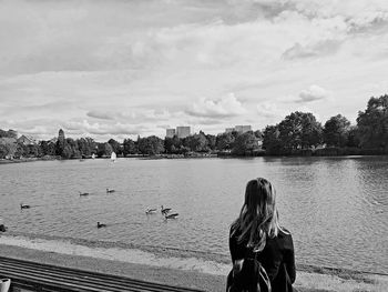 Rear view of women sitting by lake against sky