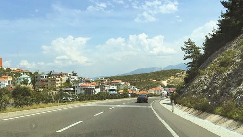 Road amidst trees and houses against sky