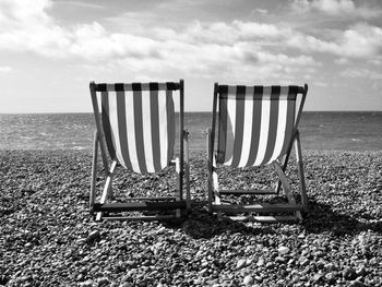 Empty chairs at beach against sky