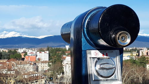 Close-up of coin-operated binoculars by buildings in city against sky