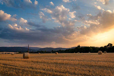 Hay bales on field against sky during sunset