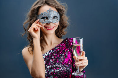 Portrait of a smiling young woman drinking glass against blue background