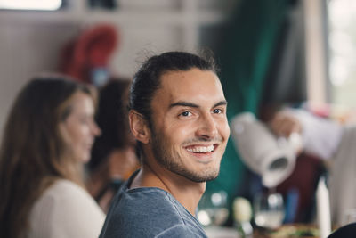 Smiling young man looking away while sitting with female friends at dining table