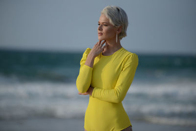 Woman looking away while standing against sea and sky