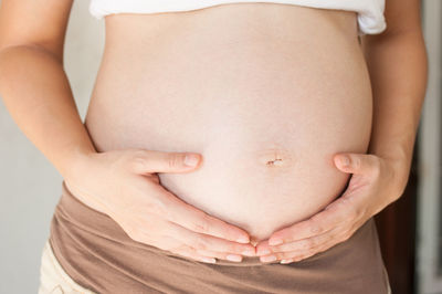 Midsection of pregnant woman with hand on stomach against white background