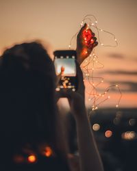 Rear view of woman photographing while holding illuminated string lights