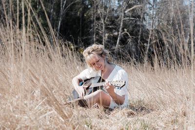 Woman sat in a field happily playing guitar in summer