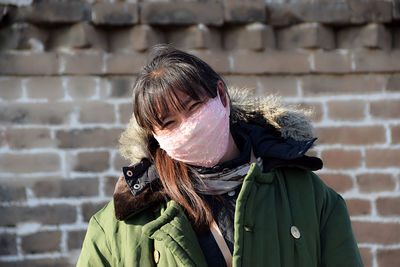 Close-up portrait of woman with pollution mask standing against brick wall