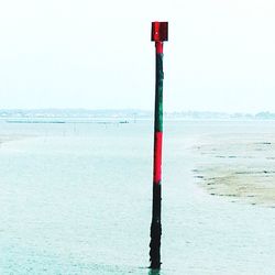 Red wooden post on beach against clear sky