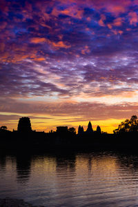 Silhouette trees by lake against romantic sky at sunset