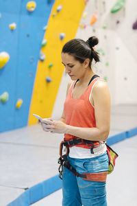 Woman using mobile phone against climbing wall