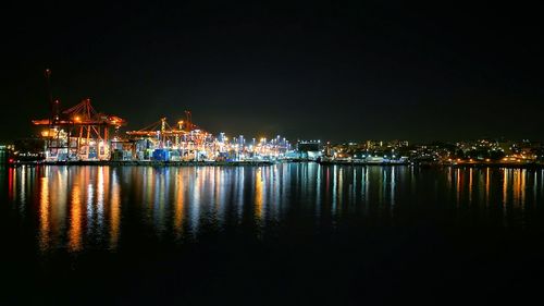 Illuminated cityscape by sea against clear sky at night