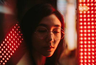 Close-up of young woman standing against illuminated city at night