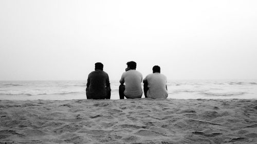 Rear view of people on beach against clear sky