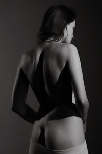 Rear view of naked woman standing against black background