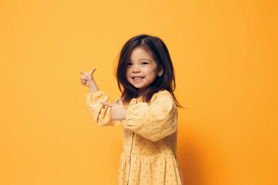 Portrait of young woman with arms raised standing against yellow background