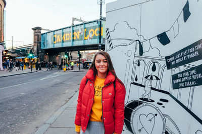 Portrait of young woman standing on sidewalk in city