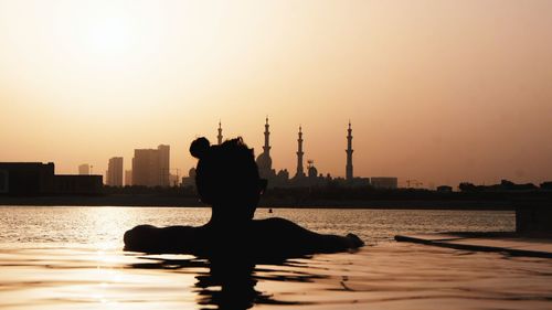 Rear view of silhouette woman in infinity pool against sky during sunset