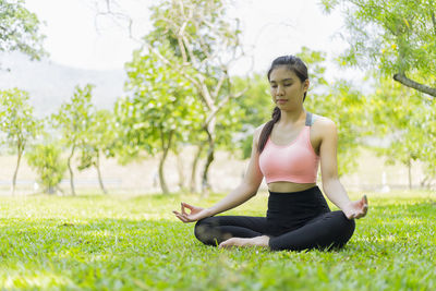Full length of woman meditating while sitting on grassy field at park