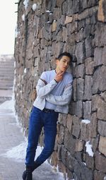 Full length portrait of young man standing by stone wall