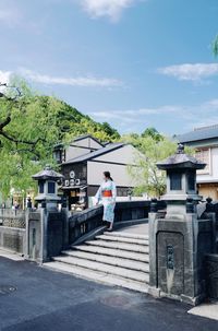 Woman standing by house against sky