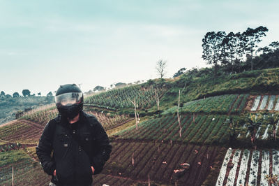 Portrait of man in helmet standing on agricultural field against sky