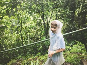 Portrait of young woman wearing raincoat in forest during rainy season