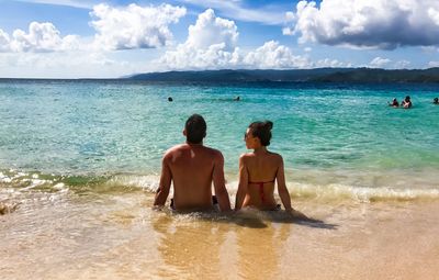 Rear view of couple sitting on shore at beach against sky