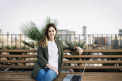 Portrait of smiling young woman sitting on railing