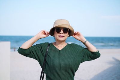 Portrait of woman wearing sunglasses and hat standing against sea