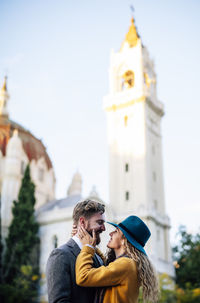 Couple kissing against tower and buildings against sky