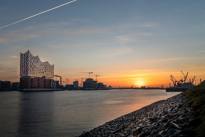 Sea by buildings against sky during sunset