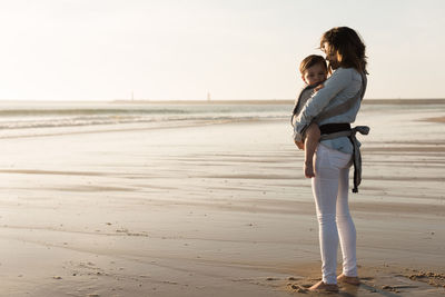 Mother carrying son while standing at beach