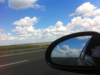 Close-up of side-view mirror against sky