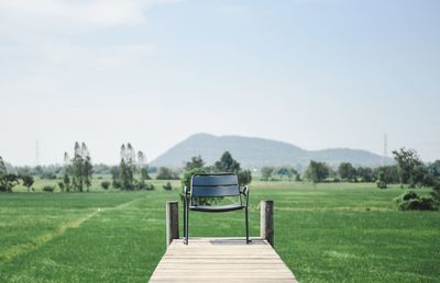 Empty park bench on field against sky