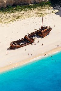 High angle view of people and shipwreck at beach on sunny day