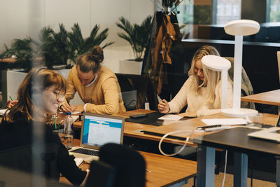 Smiling female colleagues sitting at desks with businessman in office