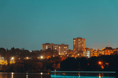 Illuminated buildings by lake against sky at night