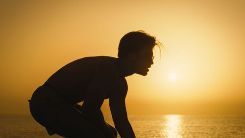 Silhouette of a boy playing american football at dawn on the beach