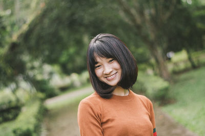 Portrait of smiling young woman standing against trees in park