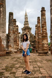 Full length portrait of young woman standing against temple