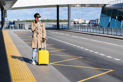 Man with suitcase talking over phone while standing on road at airport